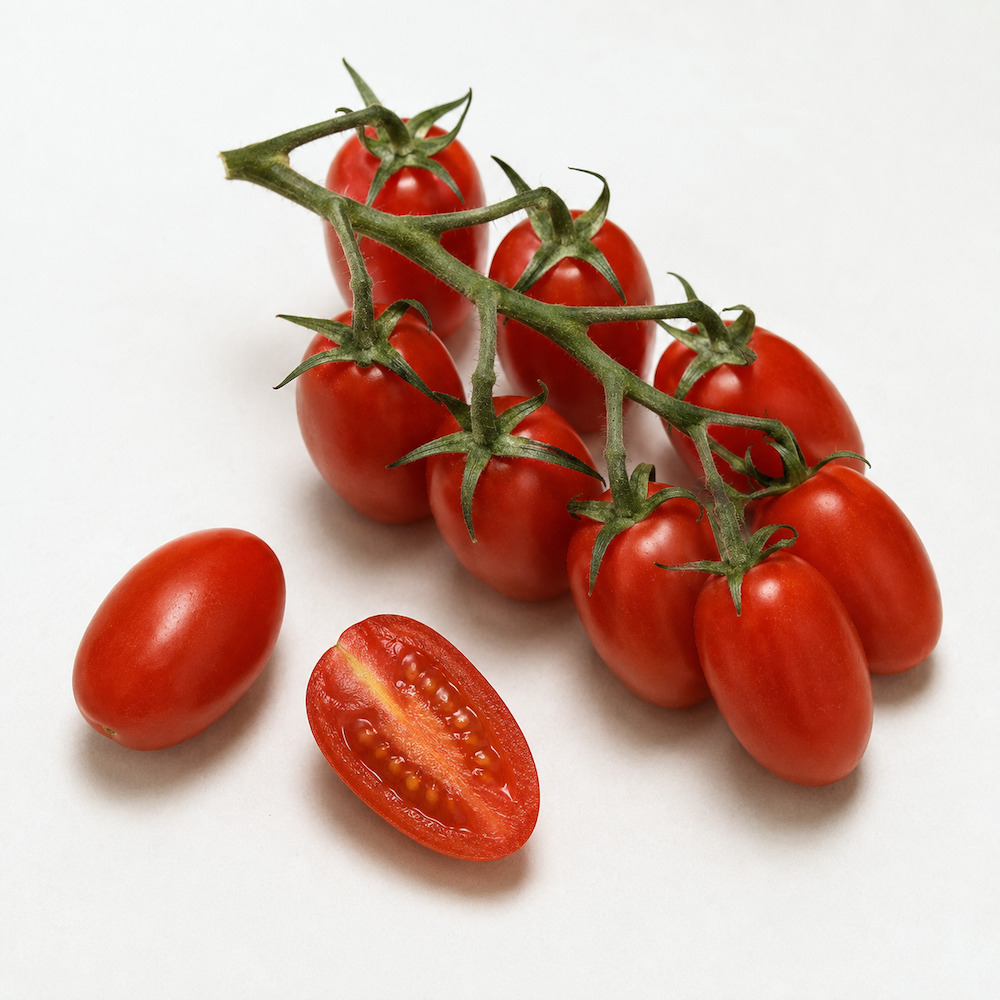 Pomodori datterino di Donnalucata sul rametto, con un frutto tagliato per il lungo che mostra la polpa densa